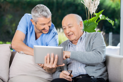 male caregiver and senior man smiling while using tablet computer